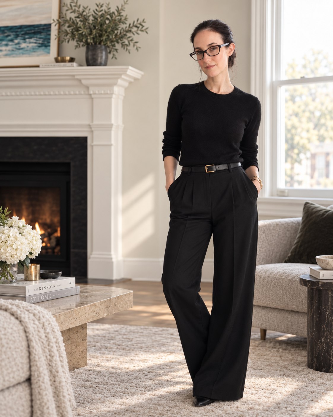 Kristin standing by the window in her living room in black knitwear and wide-leg trousers